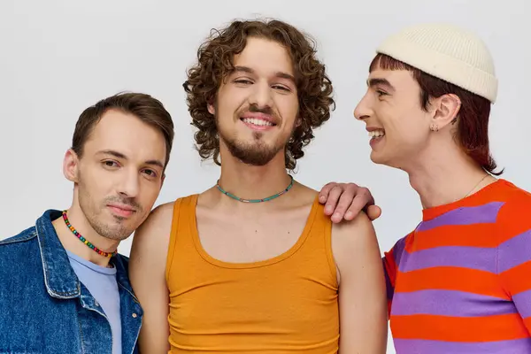 Joyous young gay men in vibrant attires posing together on gray backdrop and looking at camera — Stock Photo