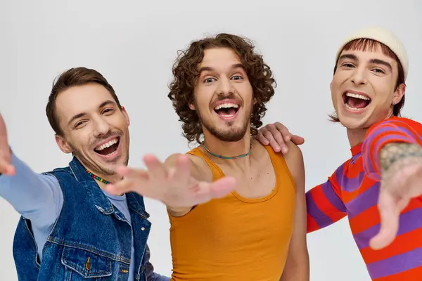 Веселые молодые геи в ярких одеждах позируют вместе на сером фоне и смотрят в камеру — стоковое фото