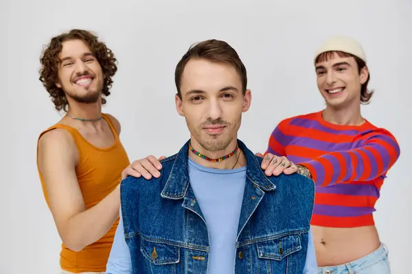 Fröhlich gut aussehende schwule Männer in lebendigen Kleidern posieren zusammen vor grauem Hintergrund und schauen in die Kamera — Stockfoto