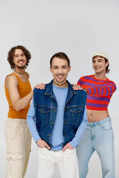 Positive handsome gay men in vibrant attires posing together on gray backdrop and looking at camera — Stock Photo