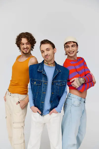 Joyful handsome gay men in vibrant attires posing together on gray backdrop and looking at camera — Stock Photo