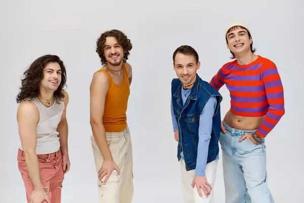 Чотири веселих добре виглядають геї в яскравих вбраннях, посміхаючись на камеру, позуючи на сірому фоні — стокове фото
