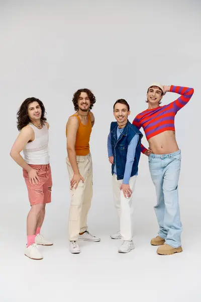 Четыре веселых симпатичных гея в ярких одеждах улыбаются в камеру, позируя на сером фоне — стоковое фото