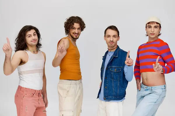 Четыре симпатичных гомосексуалиста в ярких одеждах улыбаются в камеру, позируя на сером фоне — стоковое фото