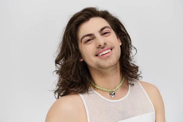 Радостный привлекательный гей с длинными волосами в повседневной одежде улыбаясь в камеру на сером фоне — стоковое фото