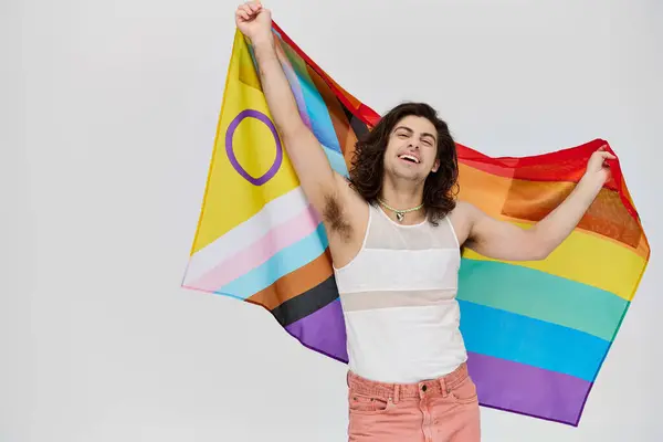 Atractivo alegre gay hombre con largo oscuro pelo posando con arco iris bandera y mirando cámara - foto de stock