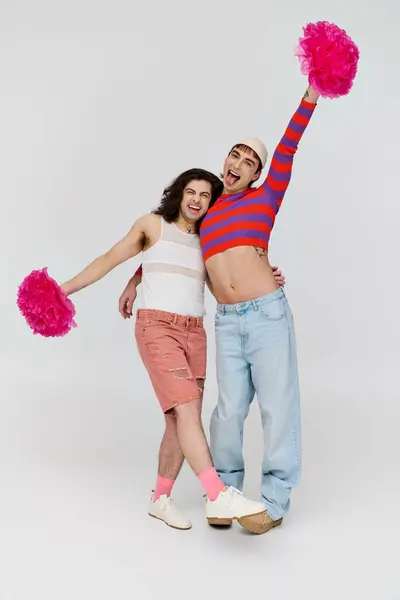Cheerful young gay men in casual vivid attires posing happily with pom poms and looking at camera — Stock Photo