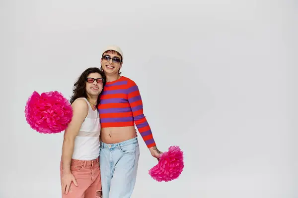 Ansprechende lustige schwule Männer in lebendigen Kleidern mit Sonnenbrille posieren mit Bommelmützen vor grauem Hintergrund — Stockfoto