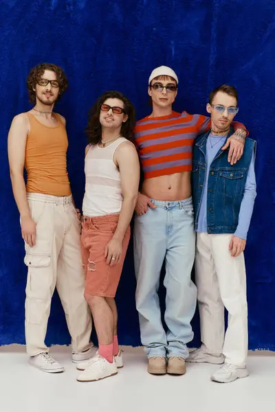 Trendy jolly attraente gay gli uomini con gli occhiali da sole in abiti vivaci posa su sfondo blu, orgoglio — Foto stock