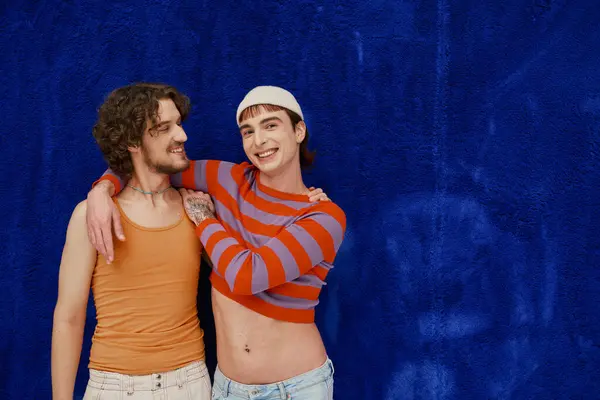 Дві веселі хороші геї в яскравому одязі позують на темно-синьому фоні, місяць гордості — стокове фото