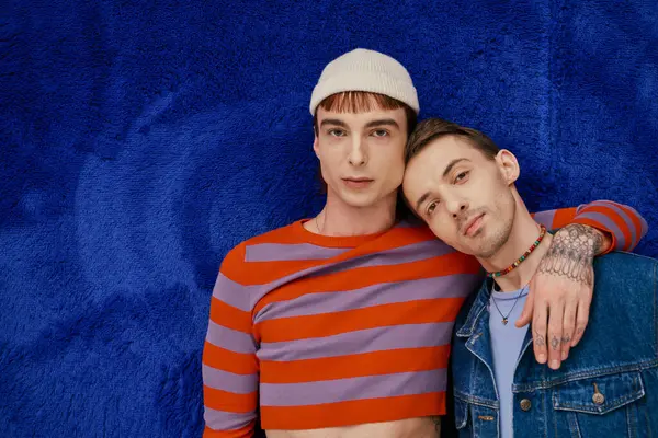 Dos feliz bien parecido gay los hombres en vibrante ropa posando en oscuro azul telón de fondo, orgullo mes - foto de stock