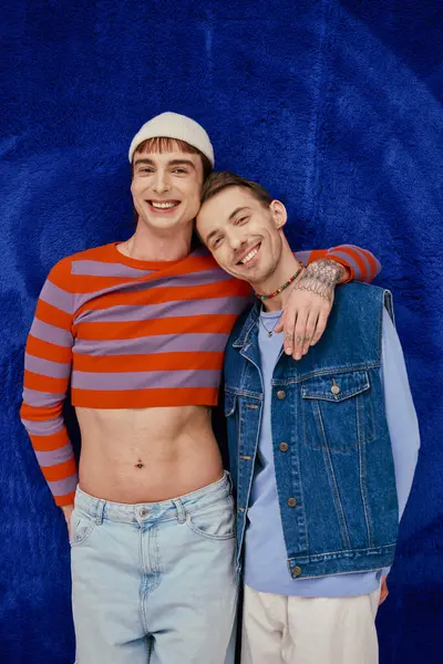 Two positive good looking gay men in vibrant clothes posing on dark blue backdrop, pride month — Stock Photo