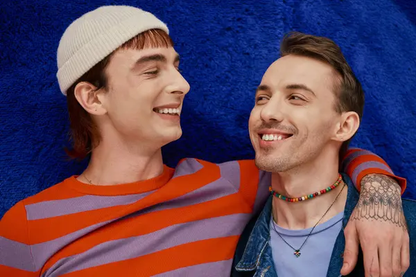 Two cheerful good looking gay men in vibrant clothes posing on dark blue backdrop, pride month — Stock Photo