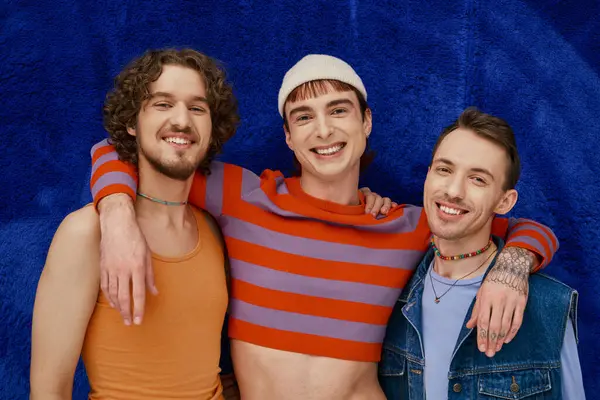 Three modish appealing merry gay friends in cozy attires posing on dark blue backdrop, pride month — Stock Photo