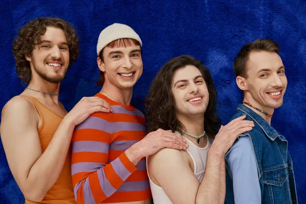 Vier freudig ansprechende stilvolle schwule Freunde in alltäglichen hellen Kleidern vor blauem Hintergrund, stolzer Monat — Stockfoto