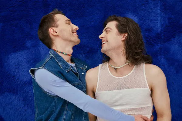Задоволені привабливі елегантні гей-друзі в затишному вбранні на темно-синьому фоні, гордість місяця — стокове фото