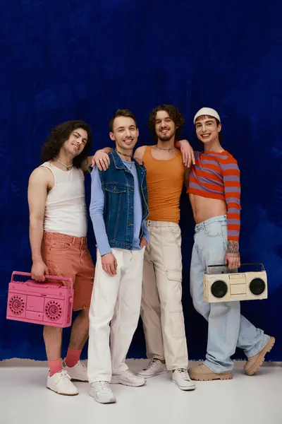 Quatre joyeux beaux hommes gays élégants dans des tenues décontractées posant avec des magnétophones, mois de fierté — Photo de stock