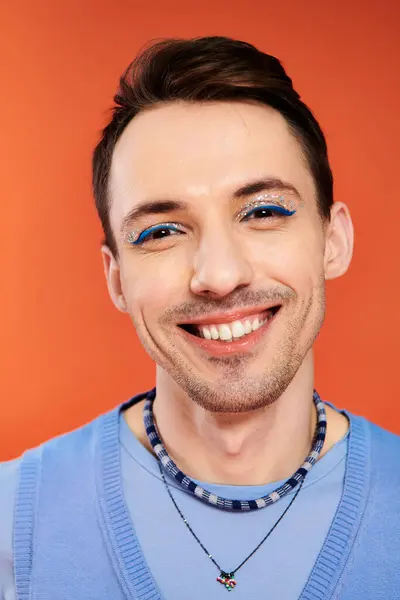 Jolly attractive stylish gay man with vibrant makeup posing on orange backdrop, pride month — Stock Photo