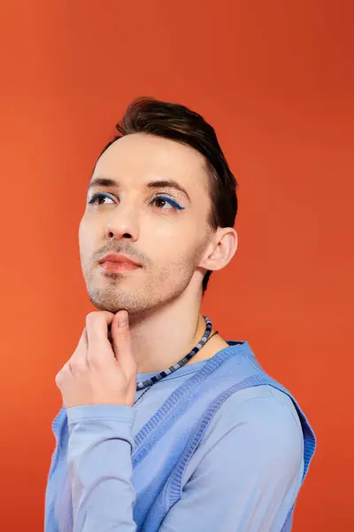 Alegre atractivo elegante gay hombre con vibrante maquillaje posando en naranja telón de fondo, orgullo mes - foto de stock