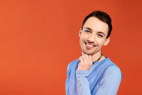 Cheerful attractive stylish gay man with vibrant makeup posing on orange backdrop, pride month — Stock Photo