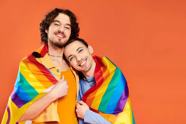 Contento atractivo jóvenes gay hombres en acogedor trajes con arco iris bandera en naranja telón de fondo, orgullo mes - foto de stock