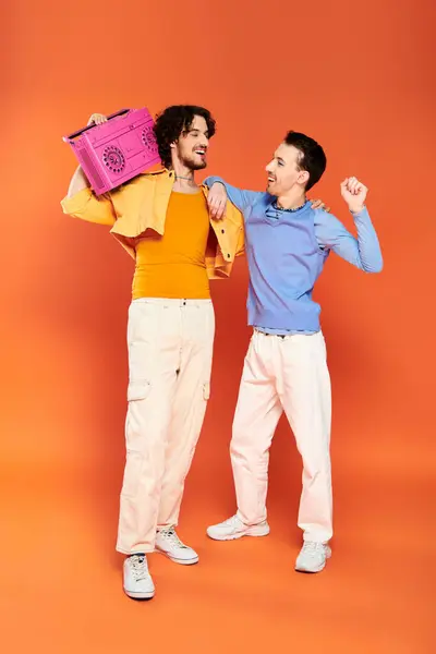 Two positive attractive gay men in vibrant cozy attire posing with tape recorder, pride month — Stock Photo