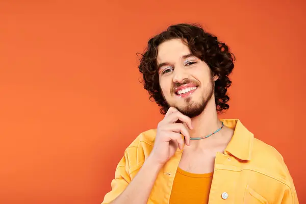 Joyeux attrayant gay l'homme avec sombre cheveux et vibrant maquillage posant sur fond orange, fierté mois — Photo de stock