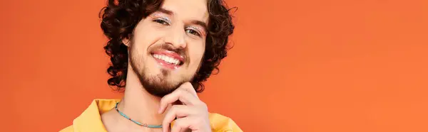 Appealing jolly gay man with dark hair and makeup posing on orange backdrop, pride month, banner — Stock Photo