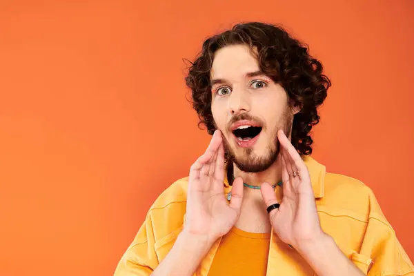 Joyeux attrayant gay homme avec les cheveux noirs et vibrant maquillage posant sur fond orange, mois de fierté — Photo de stock