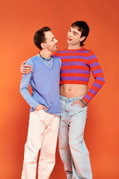 Glücklich attraktive homosexuelle Freunde mit lebhaftem Make-up posieren zusammen auf orangefarbenem Hintergrund, stolzer Monat — Stockfoto