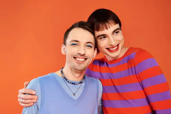 Alegre atractivo gay amigos con vívido maquillaje posando juntos en naranja telón de fondo, orgullo mes - foto de stock
