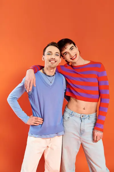 Alegre atractivo gay amigos con vívido maquillaje posando juntos en naranja telón de fondo, orgullo mes - foto de stock