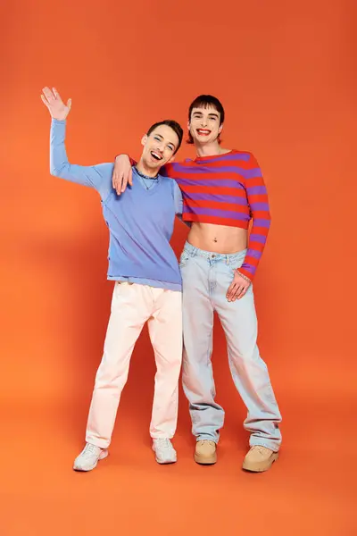Веселые привлекательные друзья-геи с ярким макияжем позируют вместе на оранжевом фоне, месяц гордости — стоковое фото