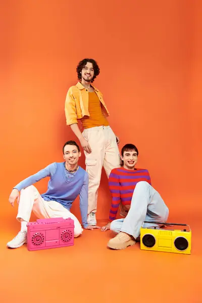 Tres alegre atractivo gay amigos en vívido atuendo posando con cinta grabadoras, orgullo mes - foto de stock
