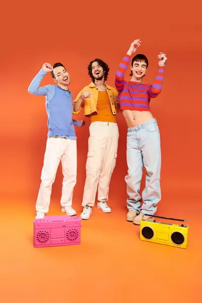 Три радісні привабливі гей друзі в яскравому вбранні позують з магнітофонами, місяць гордості — стокове фото