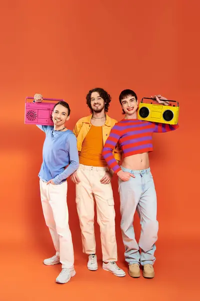 Three cheerful appealing gay friends in vivid attire posing with tape recorders, pride month — Stock Photo