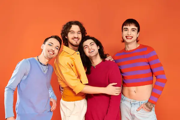 Cuatro de moda alegre gay los hombres en vibrante ropa posando juntos en naranja telón de fondo, orgullo mes - foto de stock