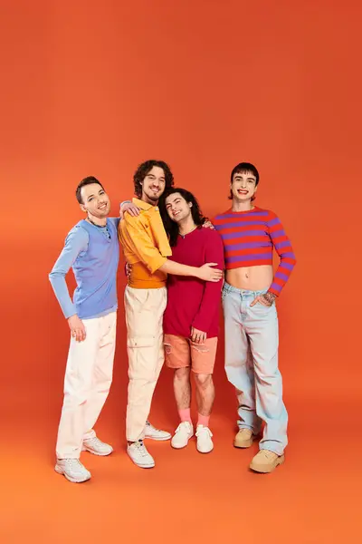Four handsome cheerful gay men in vibrant clothes posing together on orange backdrop, pride month — Stock Photo