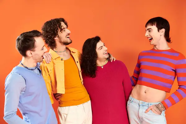 Quatre hommes gays joyeux attrayants dans des vêtements vibrants posant ensemble sur fond orange, mois de fierté — Photo de stock