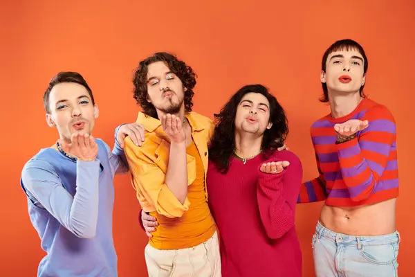 Four stylish cheerful gay men in vibrant clothes posing together on orange backdrop, pride month — Stock Photo