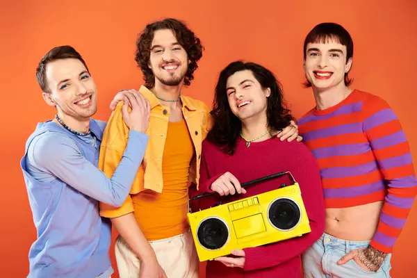 Vier freudig ansprechende schwule Freunde posieren aktiv mit Tonbandgerät auf orangefarbenem Hintergrund, stolzer Monat — Stockfoto