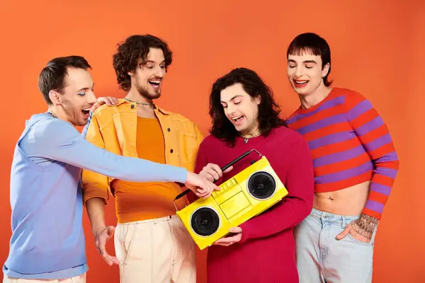 Quatro alegre bonito gay amigos posando ativamente com gravador de fita no laranja pano de fundo, orgulho mês — Fotografia de Stock
