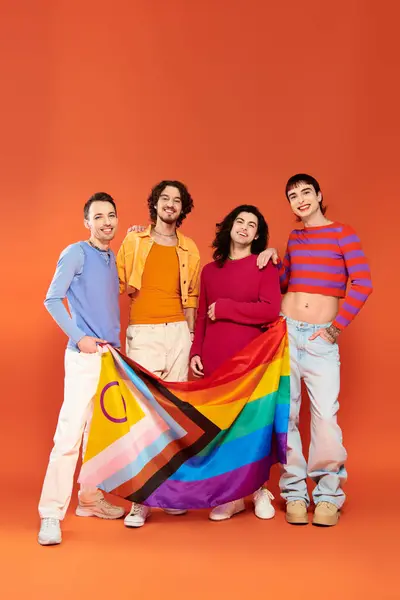 Four positive fashionable gay men in vibrant attires holding rainbow flag in front of camera, pride — Stock Photo
