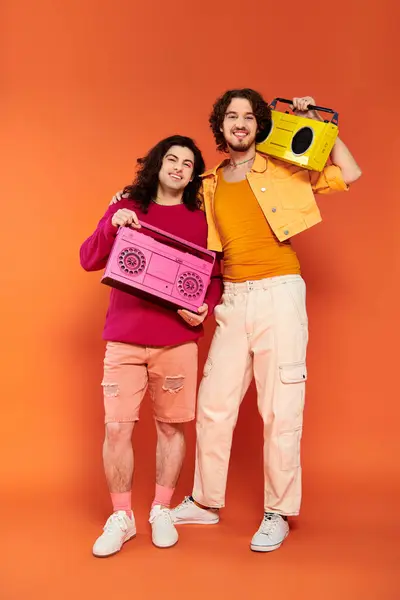 Дві радісні привабливі гей-друзі в яскравому одязі позують з магнітофонами, місяць гордості — стокове фото