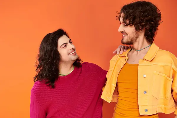 Positive junge schwule Freunde in stilvollen lebendigen Outfits posieren zusammen auf orangefarbenem Hintergrund, Stolz — Stockfoto