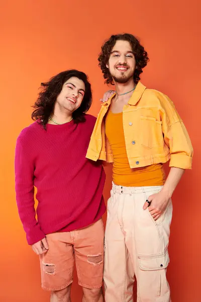 Contento jóvenes amigos gay en elegante vívido trajes posando juntos en naranja telón de fondo, orgullo - foto de stock