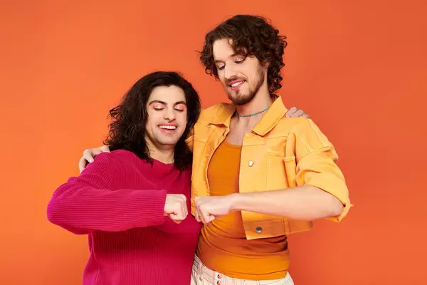 Alegre joven gay amigos en elegante vívido trajes posando juntos en naranja telón de fondo, orgullo - foto de stock