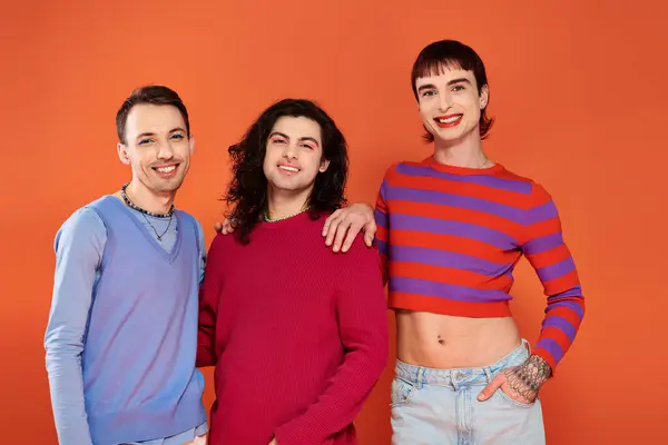 Three fashionable joyous gay friends in vivid clothes posing together on orange backdrop, pride — Stock Photo