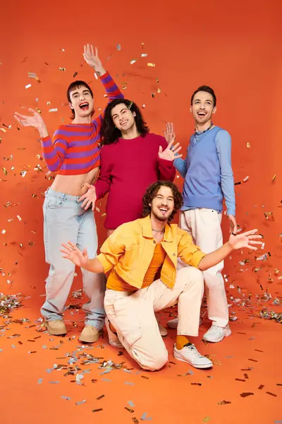 Four positive stylish gay friends in bold outfits posing actively under confetti rain, pride month — Stock Photo