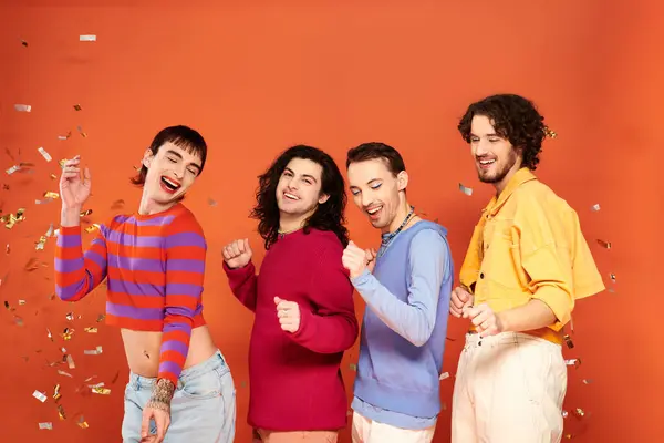Cuatro guapo alegre gay los hombres en vibrante ropa posando juntos bajo confeti lluvia orgullo mes - foto de stock
